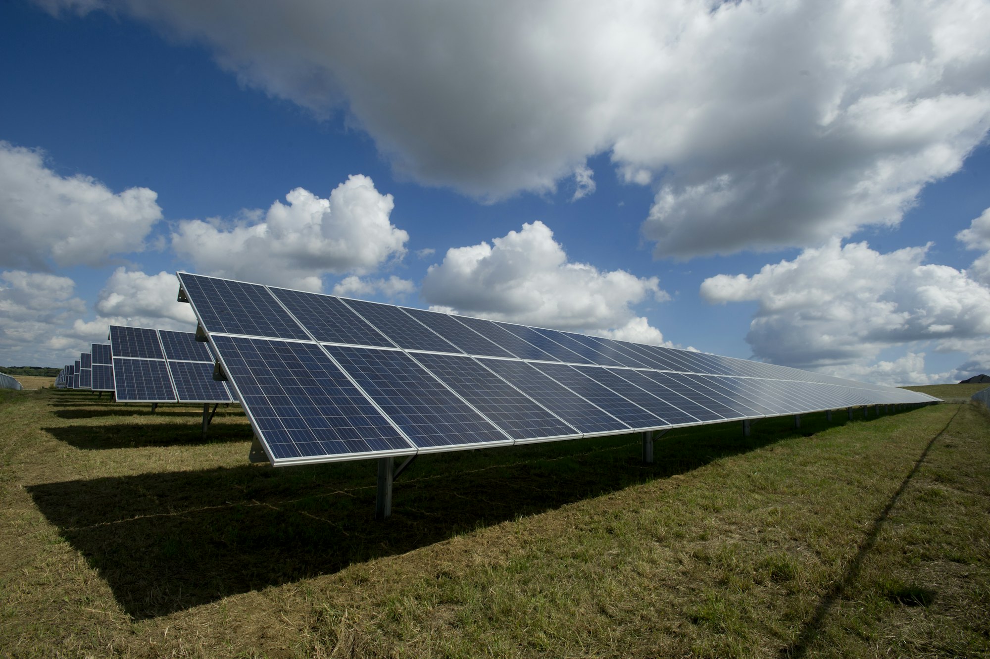 Rows of solar modules mounted in an open field under a bright sky